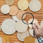 diverse monete e mano con lente d'ingrandimento