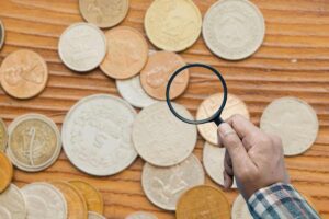 diverse monete e mano con lente d'ingrandimento